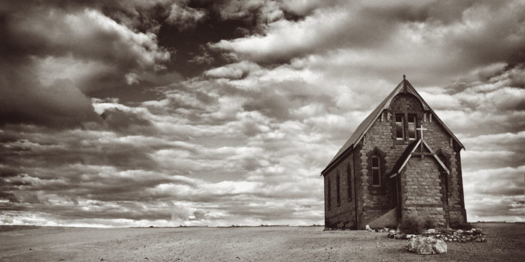 Abandoned church in the desert, with stormy skies.  Monotone image, with added grain.